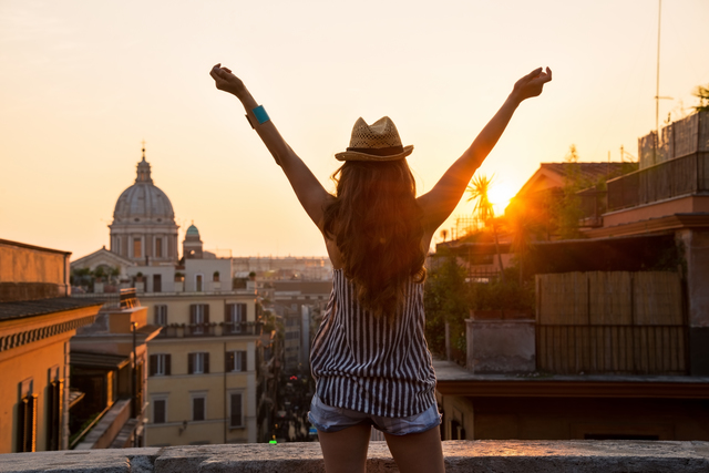 Young woman looking on rooftops of rome on sunset and rejoicing. rear view