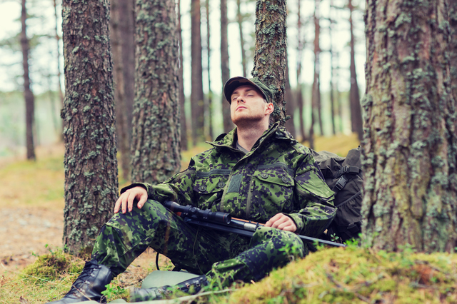 soldier or hunter with gun sleeping in forest