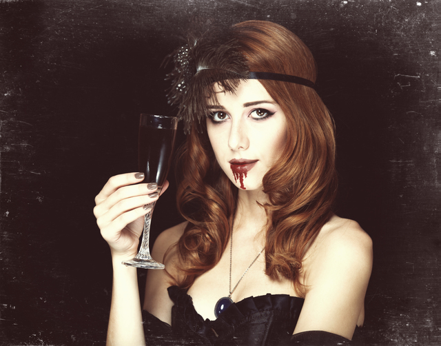Redhead vampire woman with glass of blood. Photo in vintage styl